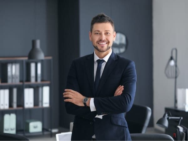 Un avvocato sorridente in abito elegante, con le braccia incrociate, rappresenta fiducia e competenza nel recupero crediti.